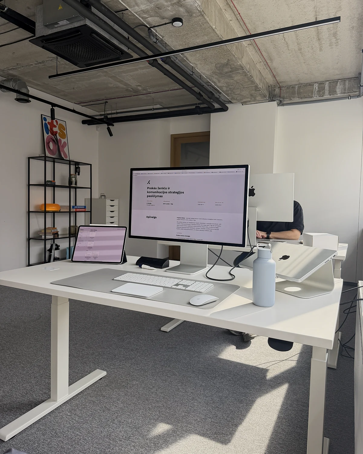 A desk in the studio with a display, a laptop and an iPad, a brand strategy proposal open on the screen